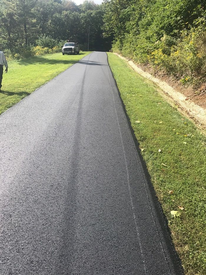 Newly paved asphalt road with green grass on both sides, a vehicle in the distance, trees.