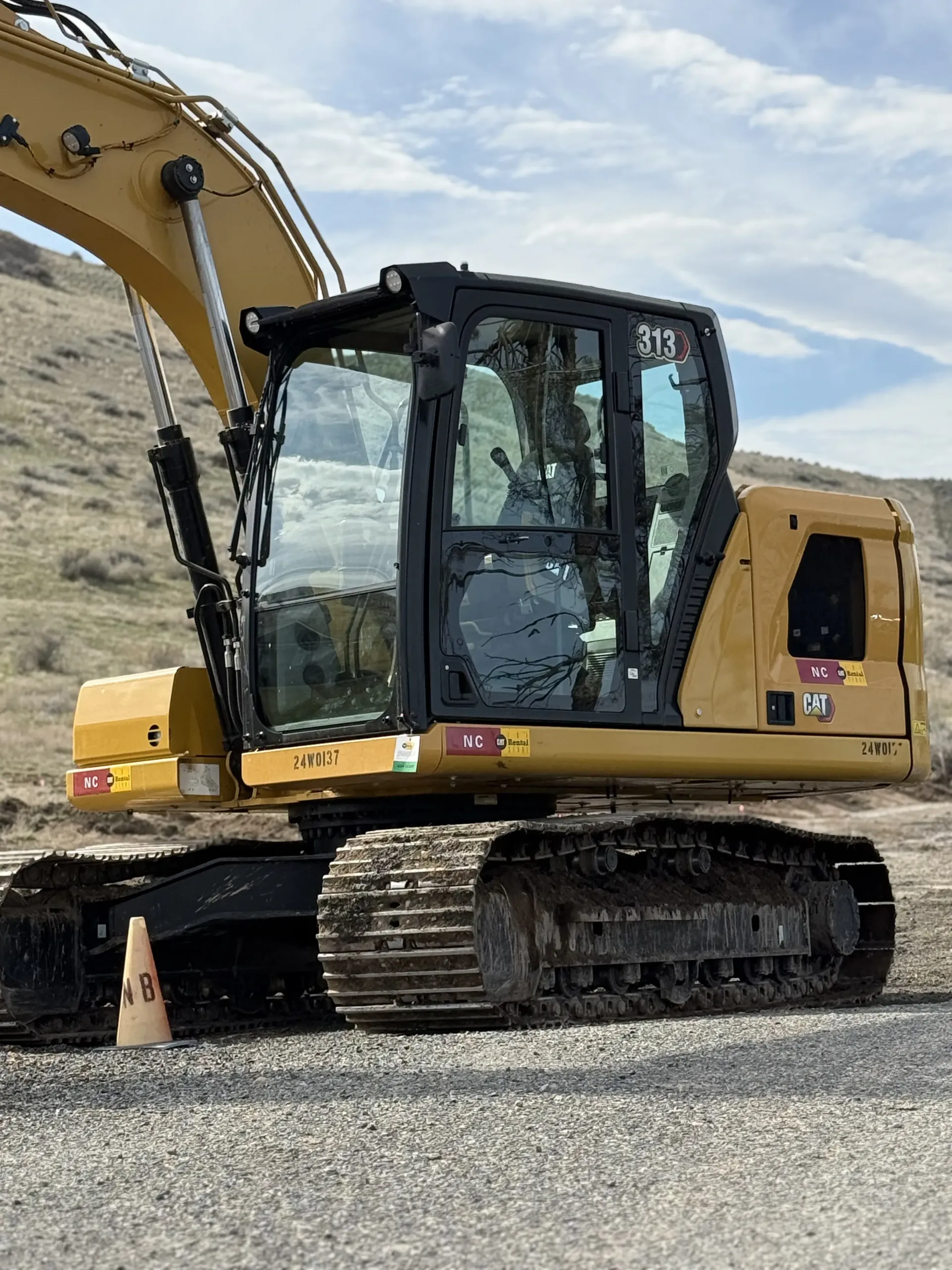 Yellow and black Caterpillar excavator parked on a gravel surface outdoors under a partly cloudy sky.