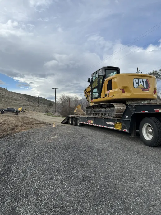 A yellow Caterpillar excavator parked on a flatbed trailer on a gravel road in a desert landscape.