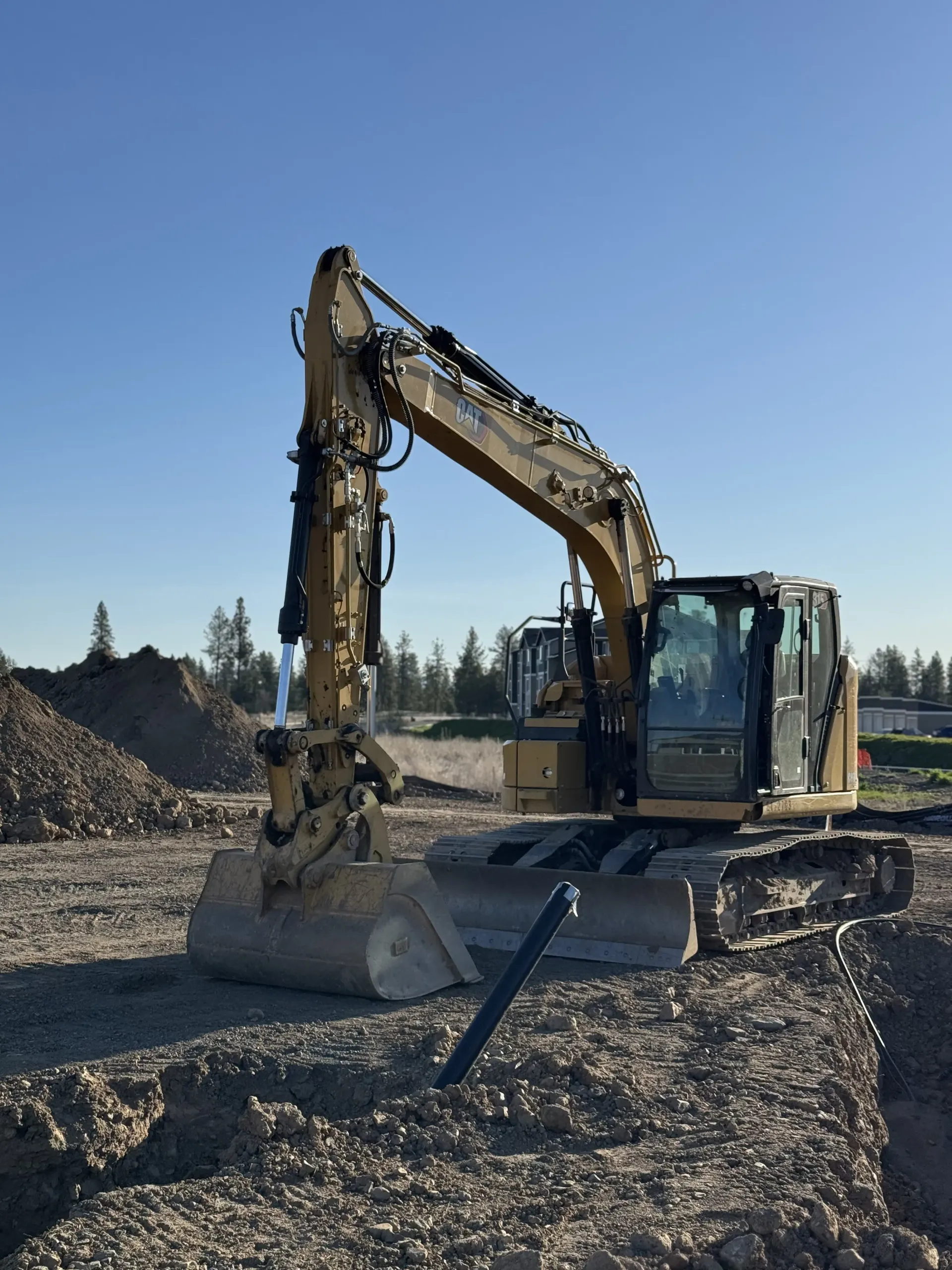 A yellow Caterpillar excavator parked on a dirt construction site against a clear blue sky.