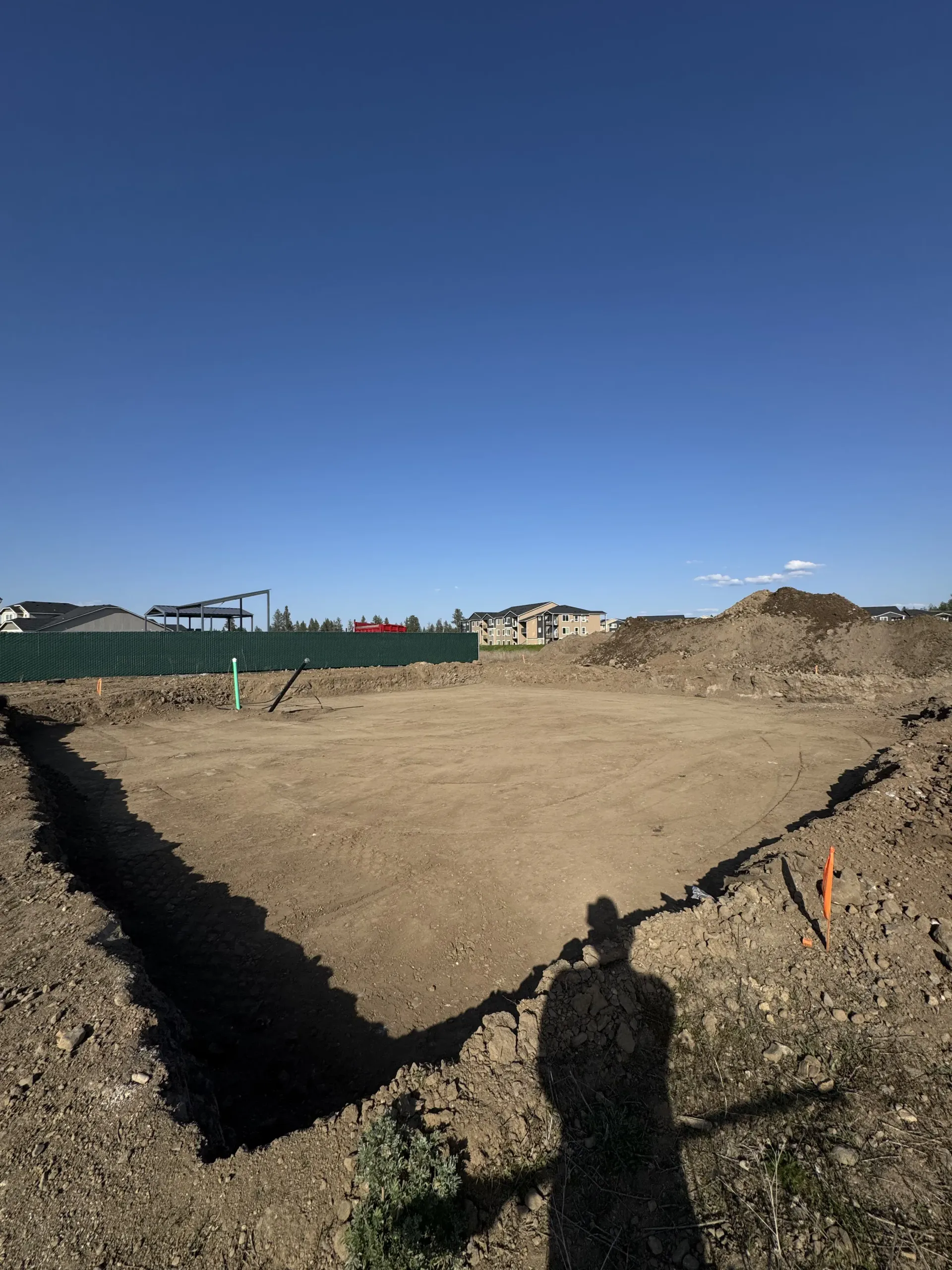 An excavated square foundation site for a new building on a sunny day with a deep blue sky above.