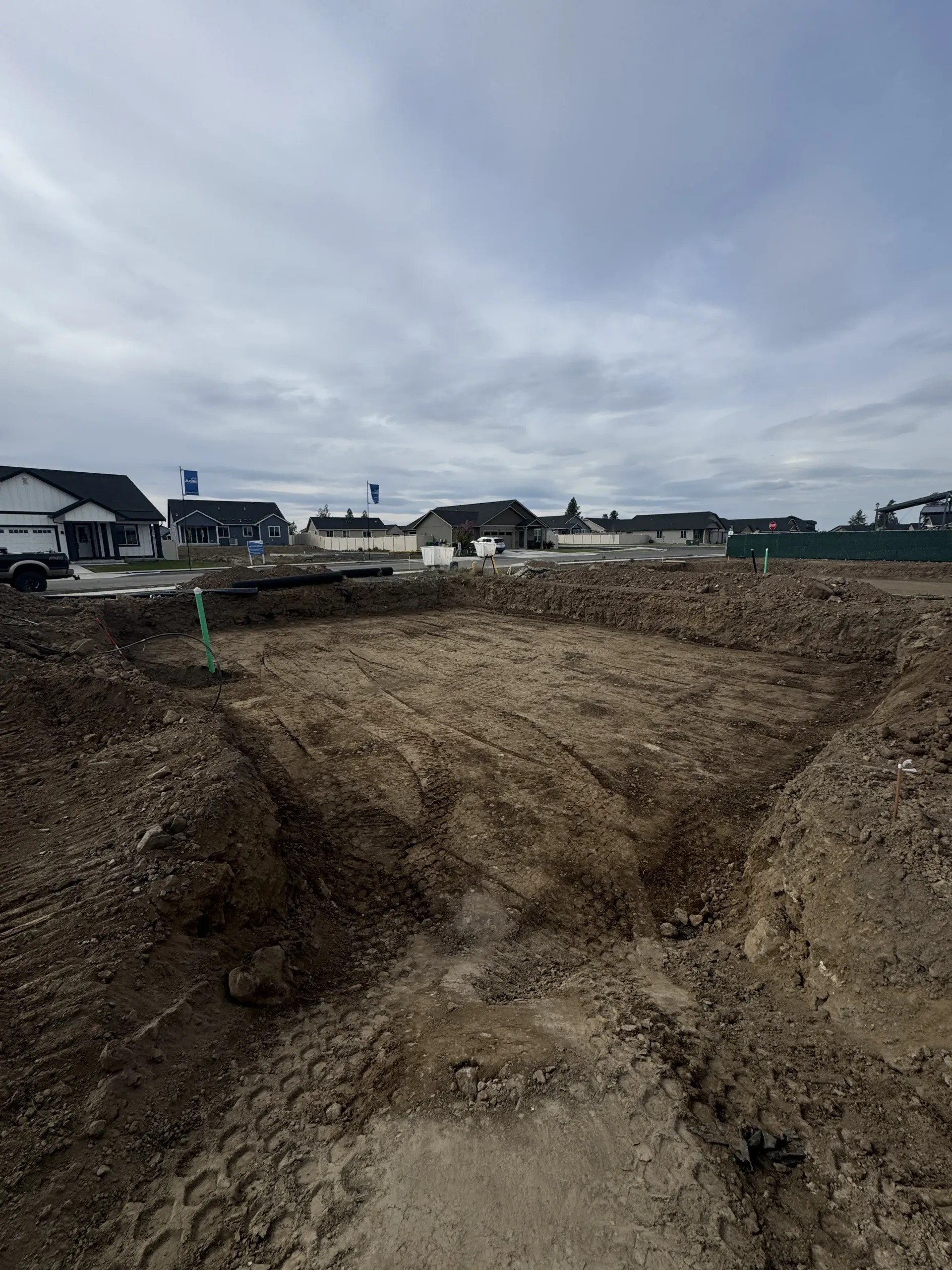 An excavated rectangular dirt foundation for a new home construction site under a cloudy sky.