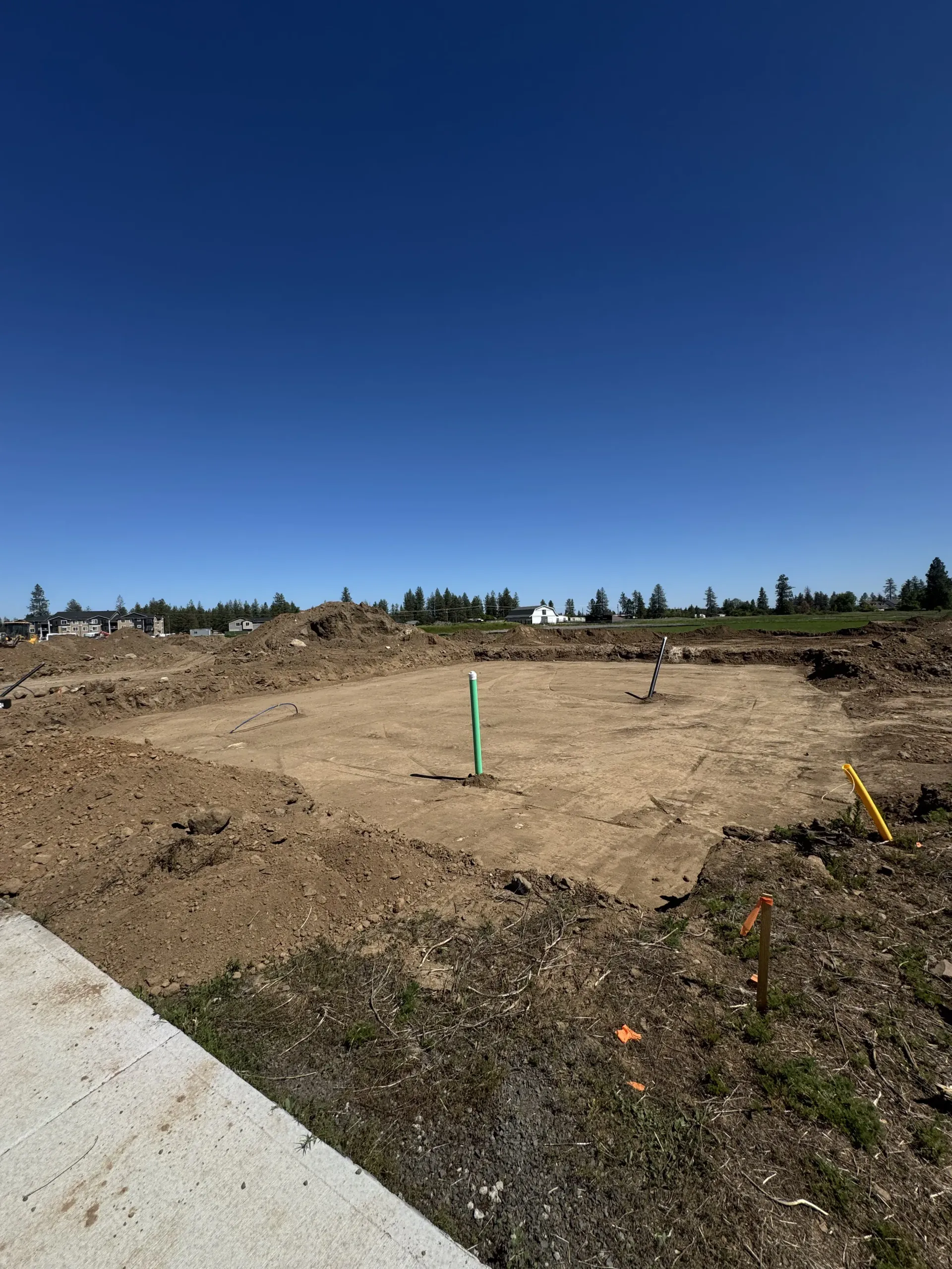 A dirt construction site for a building foundation with a green pipe sticking out under a bright blue sky.