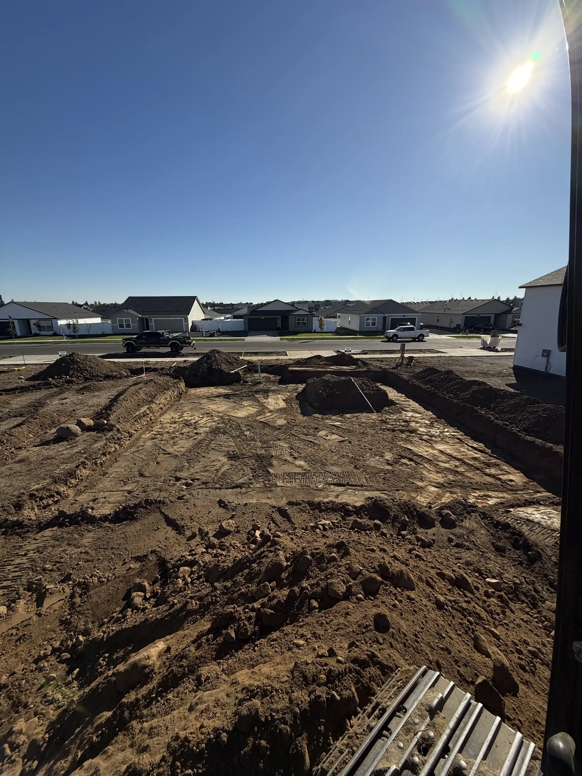 A construction site with excavated dirt trenches in the foreground under a bright, clear blue sky.
