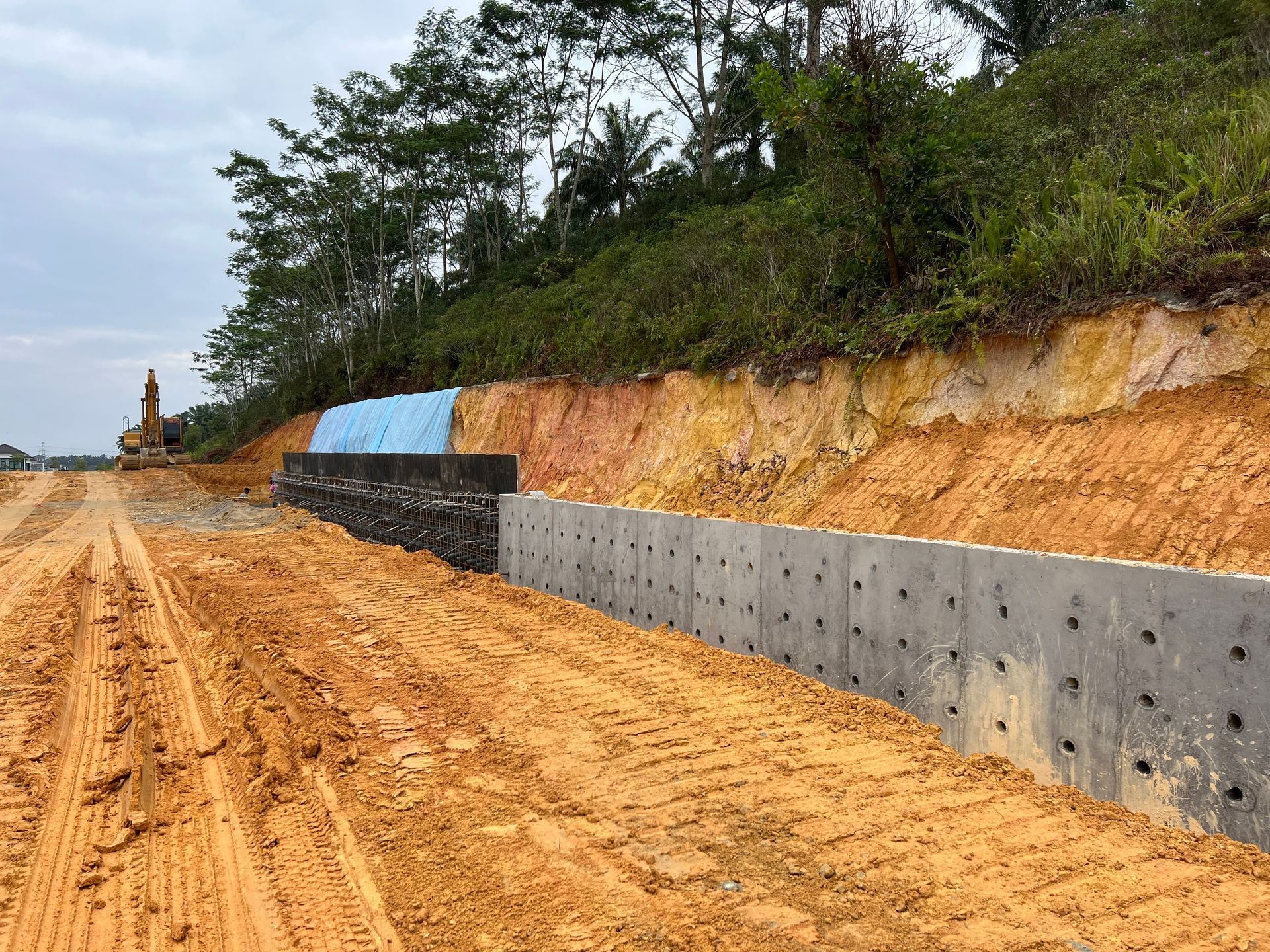 A retaining wall made of concrete blocks protects a dirt embankment along a construction site under a cloudy sky.
