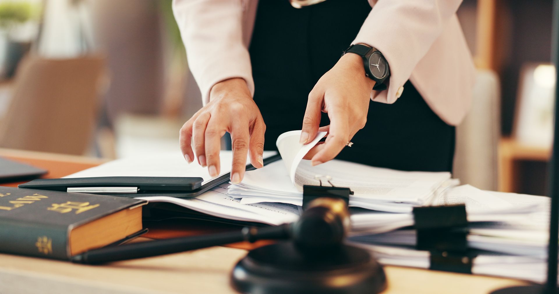Person organizing papers on a desk with books and a laptop in an office setting
