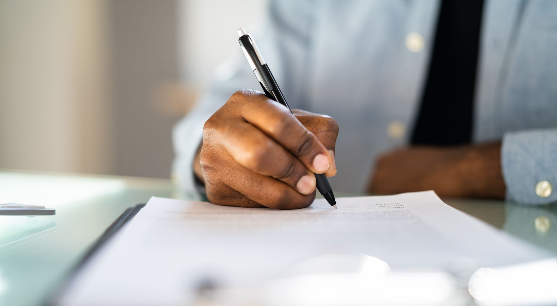 Hand holding a pen over a blank document on a desk, ready to write