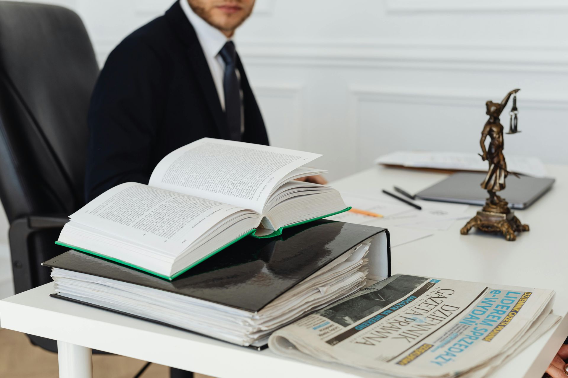 Open book and stack of documents on an office desk beside a desk sculpture and seated man