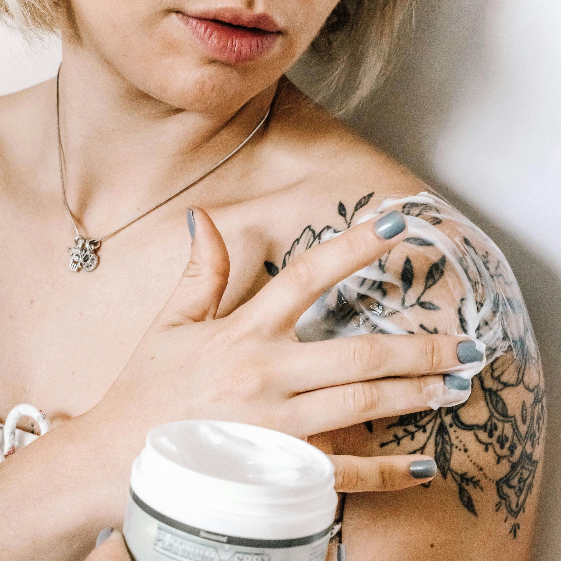 Woman applying aftercare lotion to a fresh shoulder tattoo