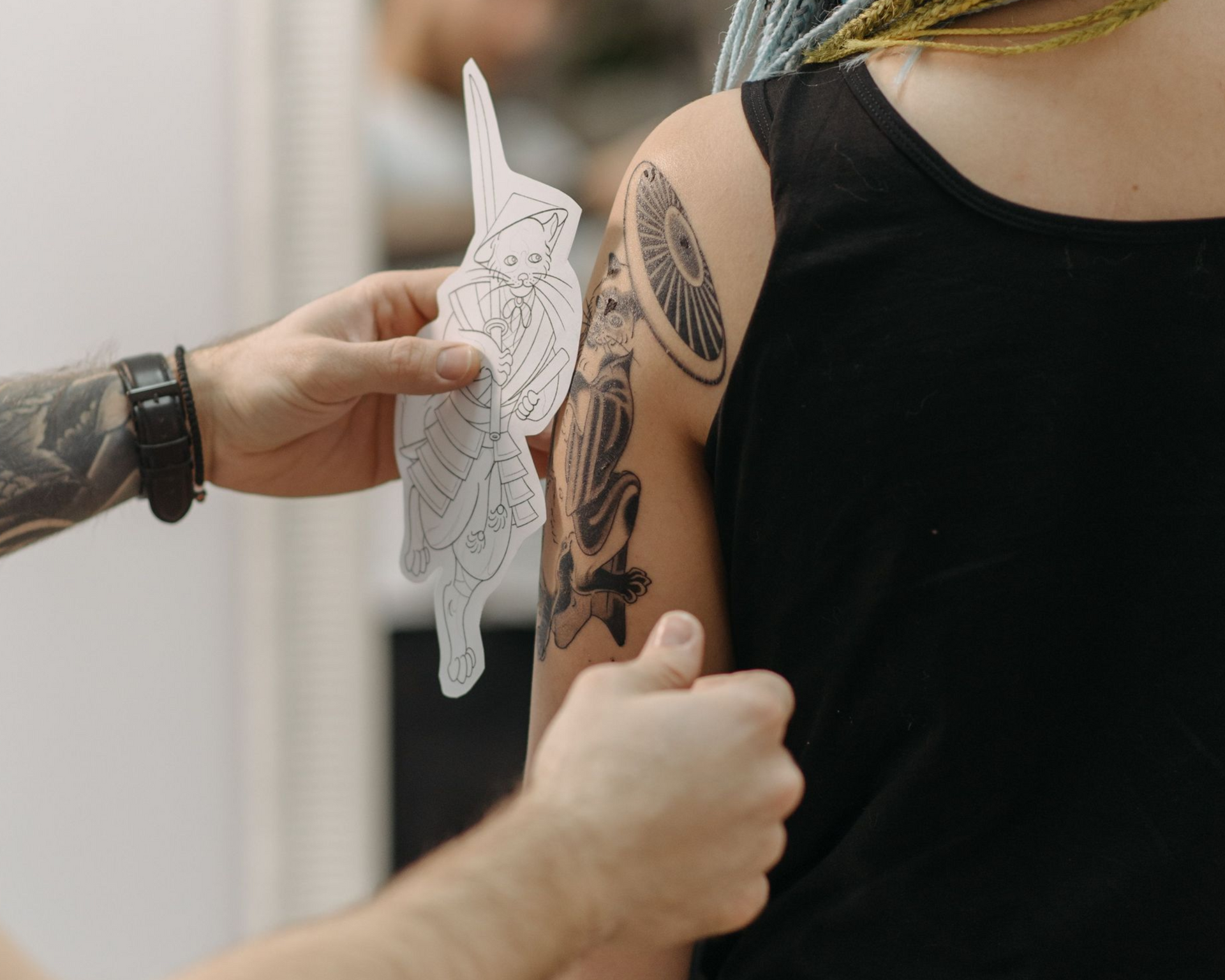 tattoo artist placing a stencil over another tattoo on someone's shoulder