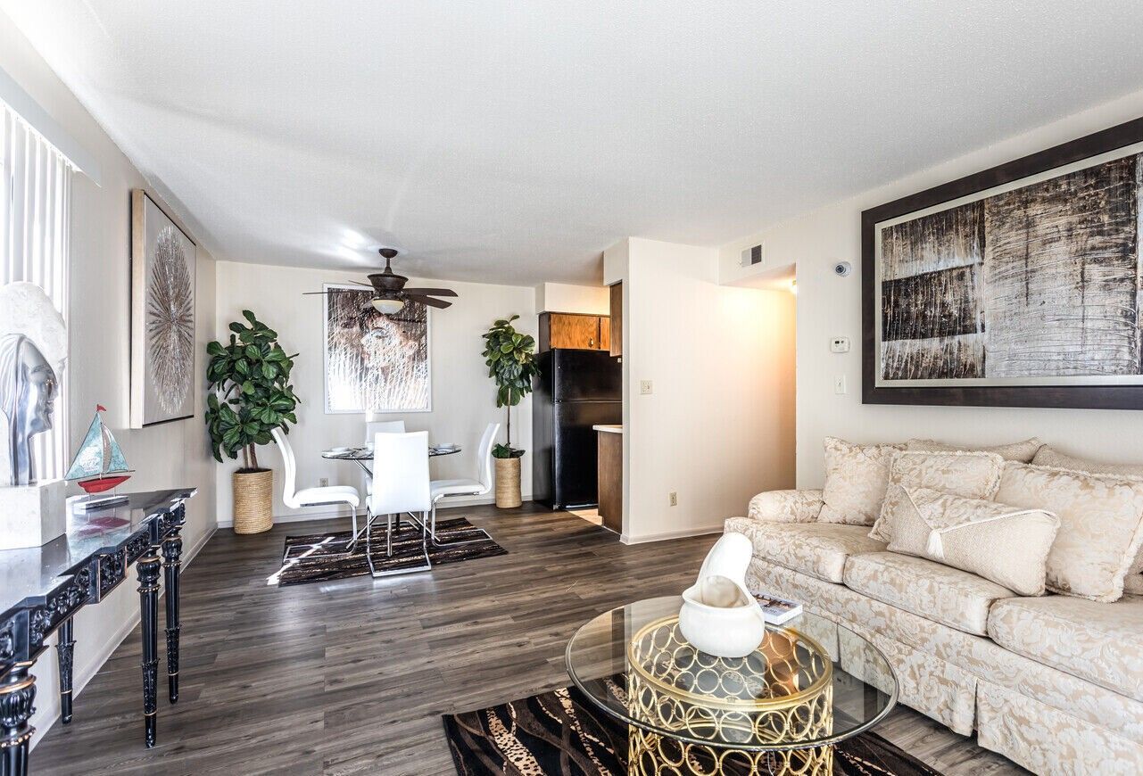 Living room with neutral tones, sofa, dining table, art, and dark wood flooring.