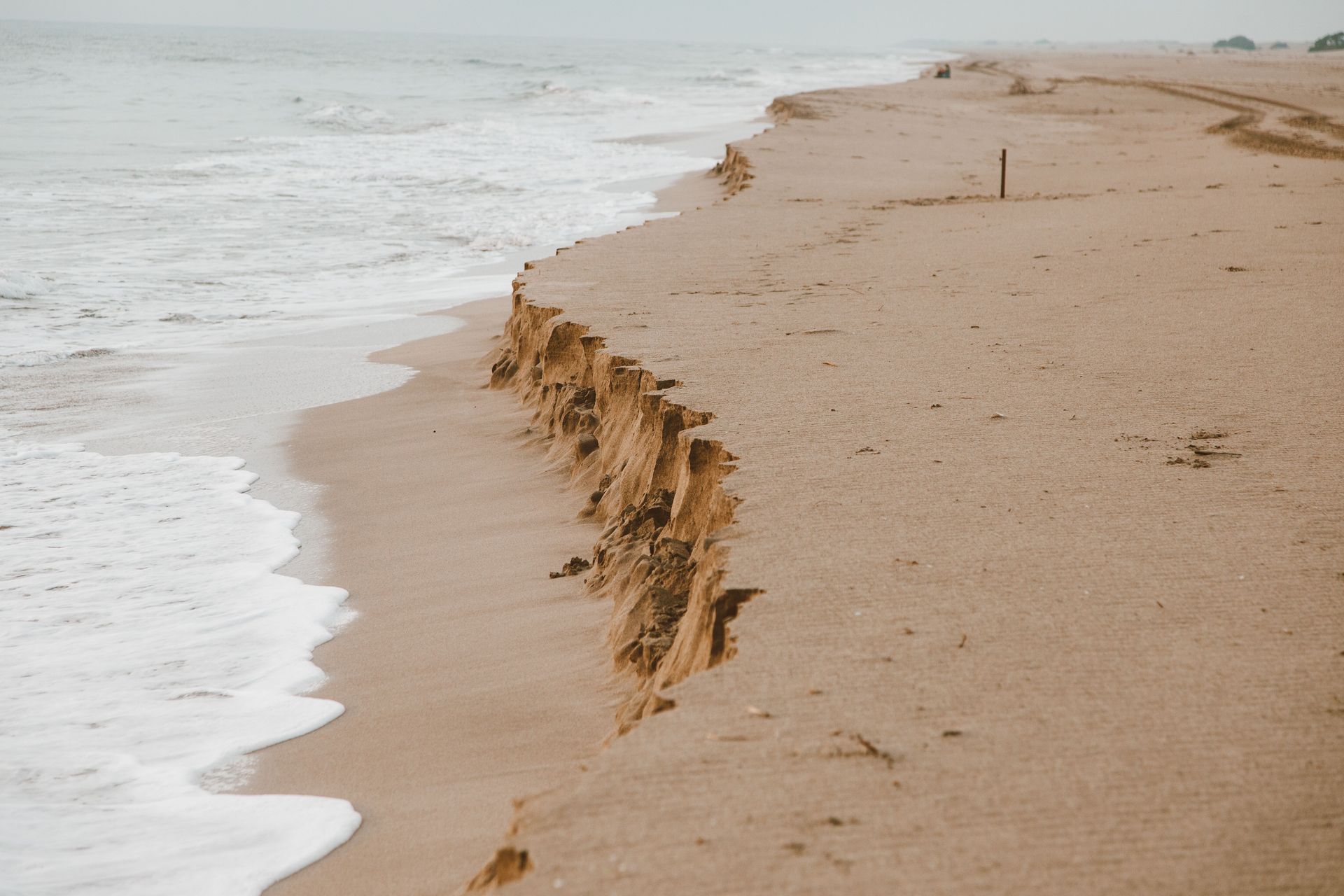 Steep sand cliff eroding into the ocean along a quiet beach