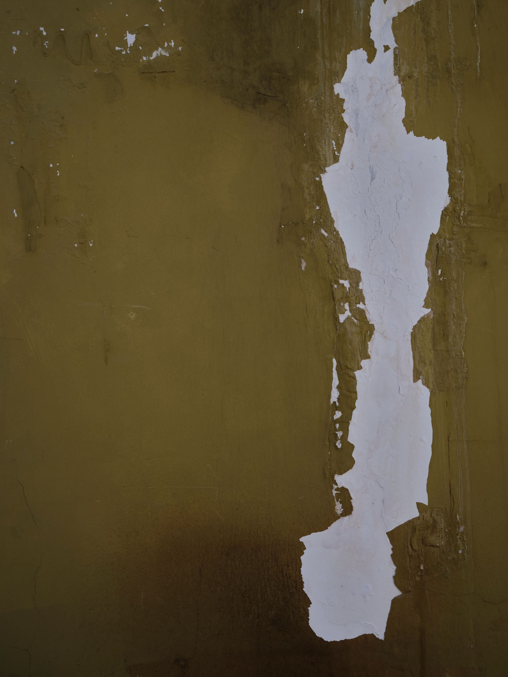 Peeling white paint on a worn olive-green wall with exposed plaster beneath