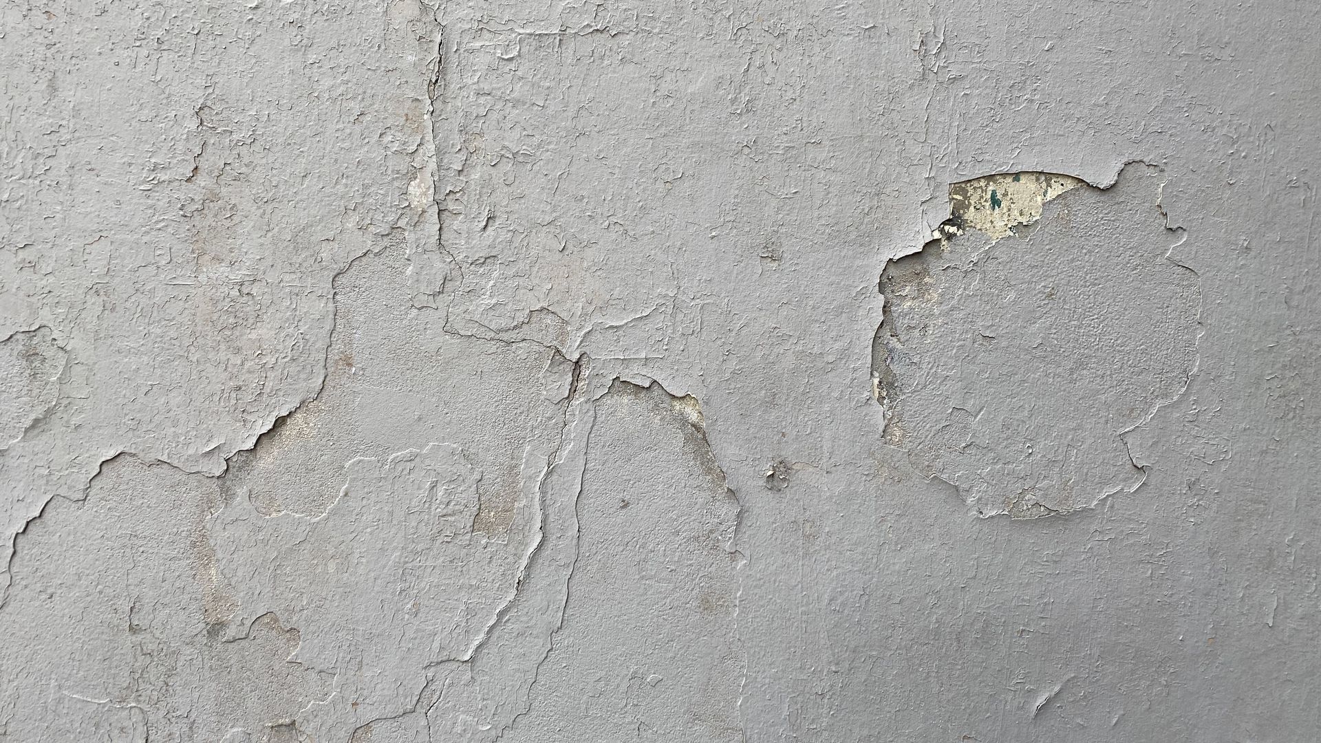 Cracked gray wall with peeling paint and exposed plaster