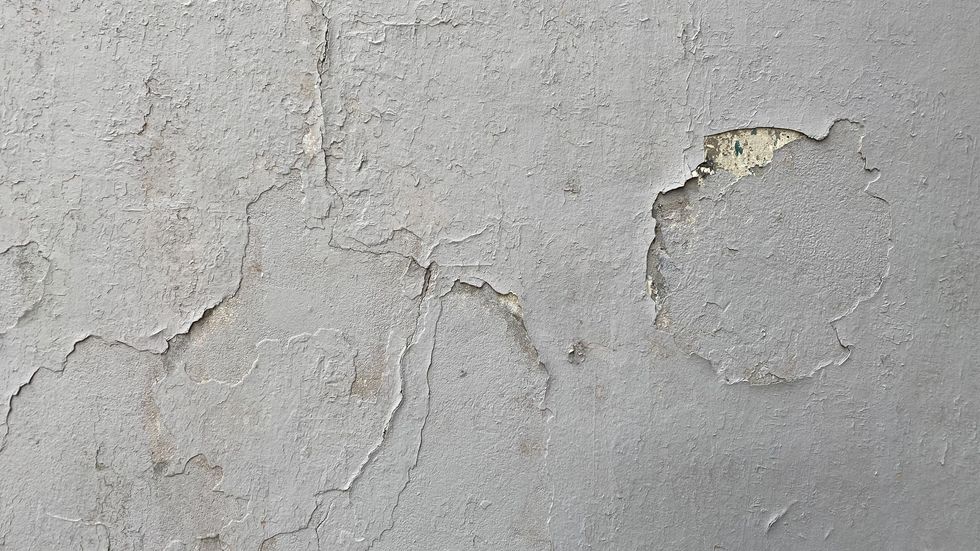 Cracked gray wall with peeling paint and exposed plaster