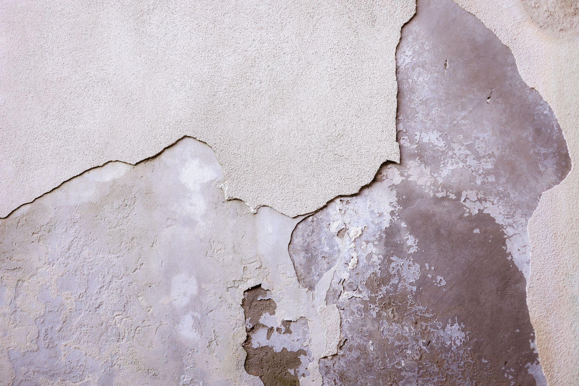 Cracked, peeling wall with gray and beige plaster damage