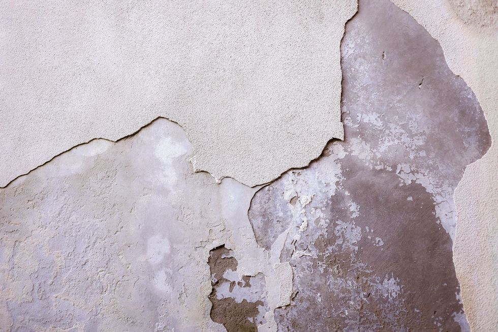 Cracked, peeling wall with gray and beige plaster damage