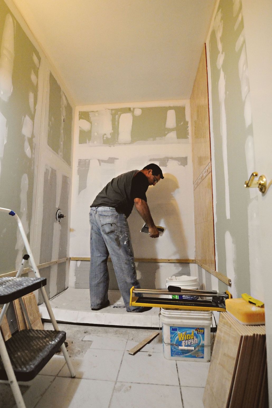 Person applying drywall compound in a partially renovated room with exposed patchwork walls.