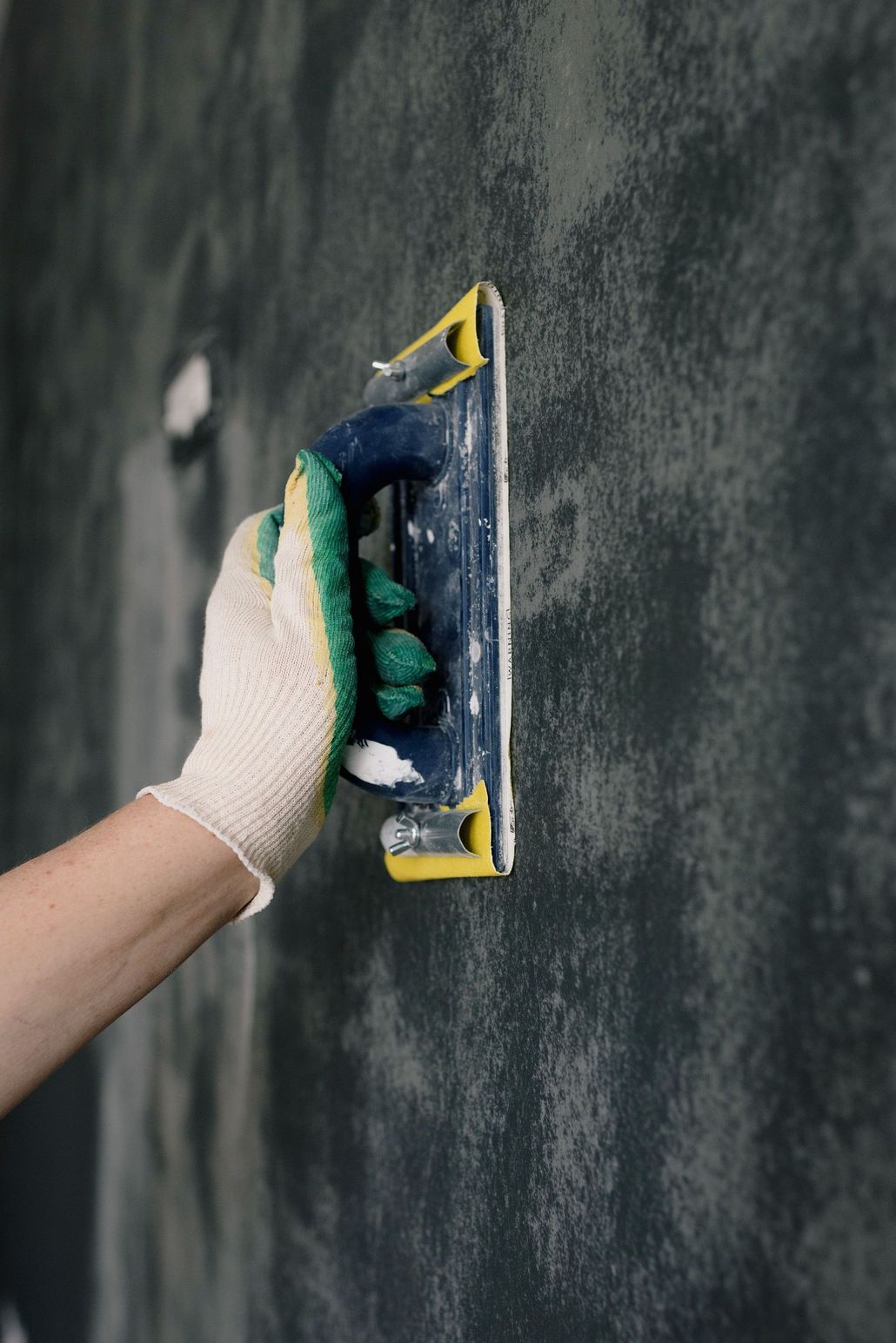 Hand sanding a dark wall with a yellow sanding block and gloved hand