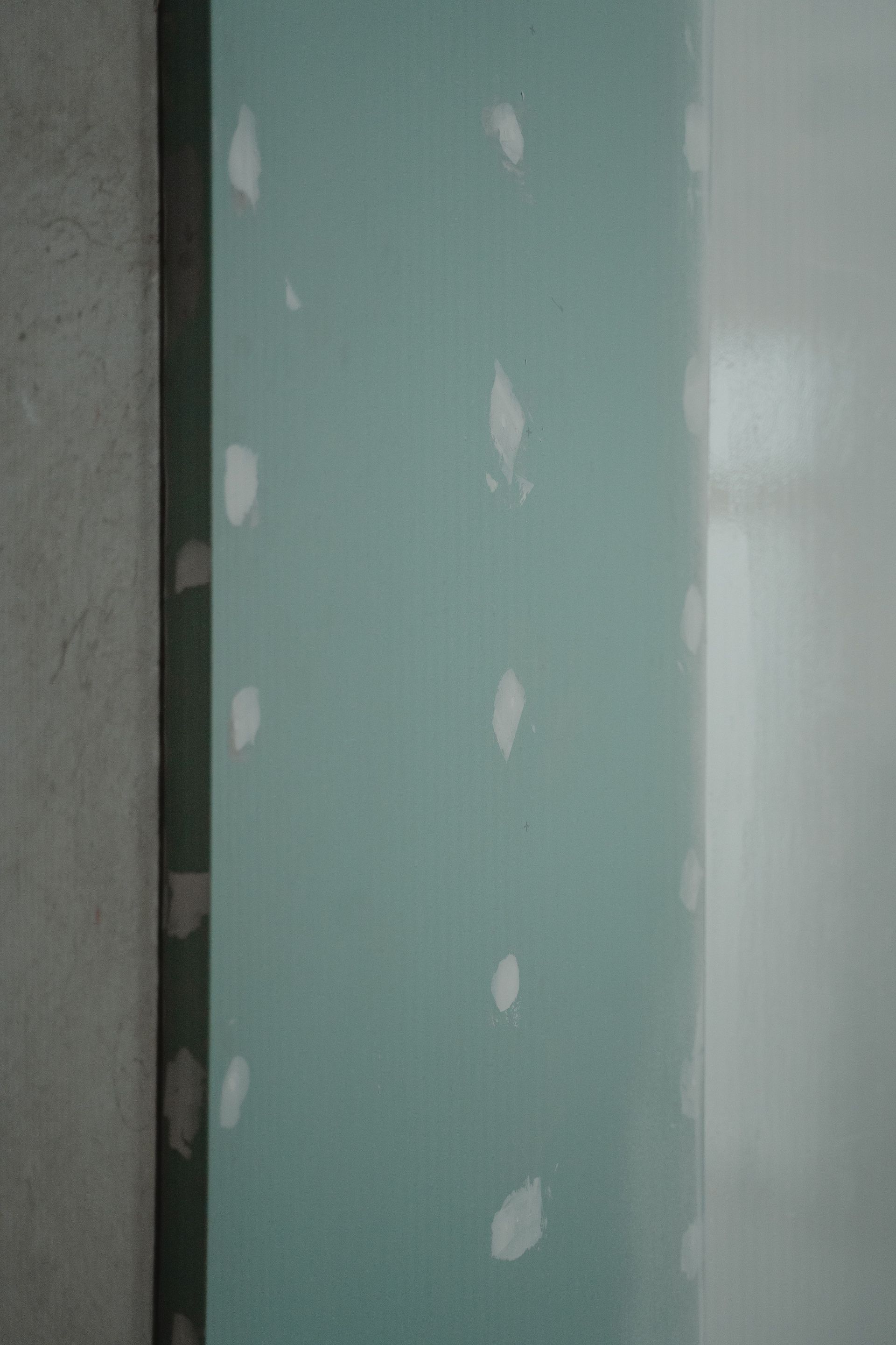 Green drywall panel with white joint compound patches near a wall corner