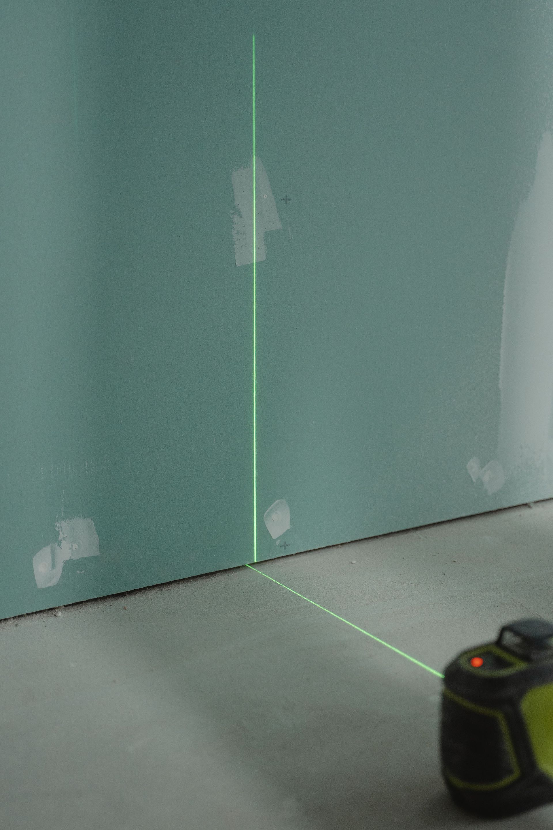 Green laser level lines on a wall and floor corner, with a tape measure in the lower right.