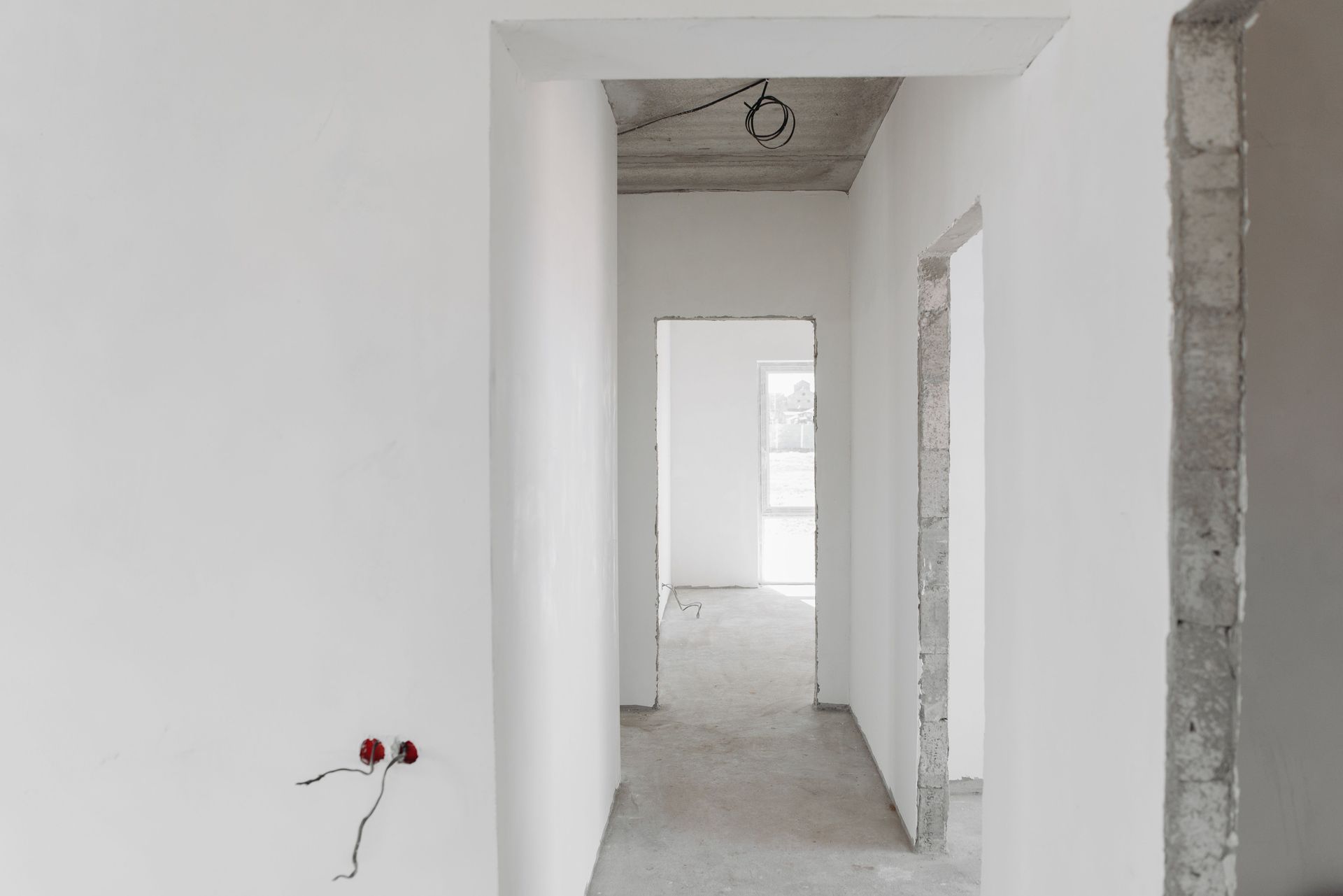 White unfinished hallway with doorways and exposed wiring in a new building.