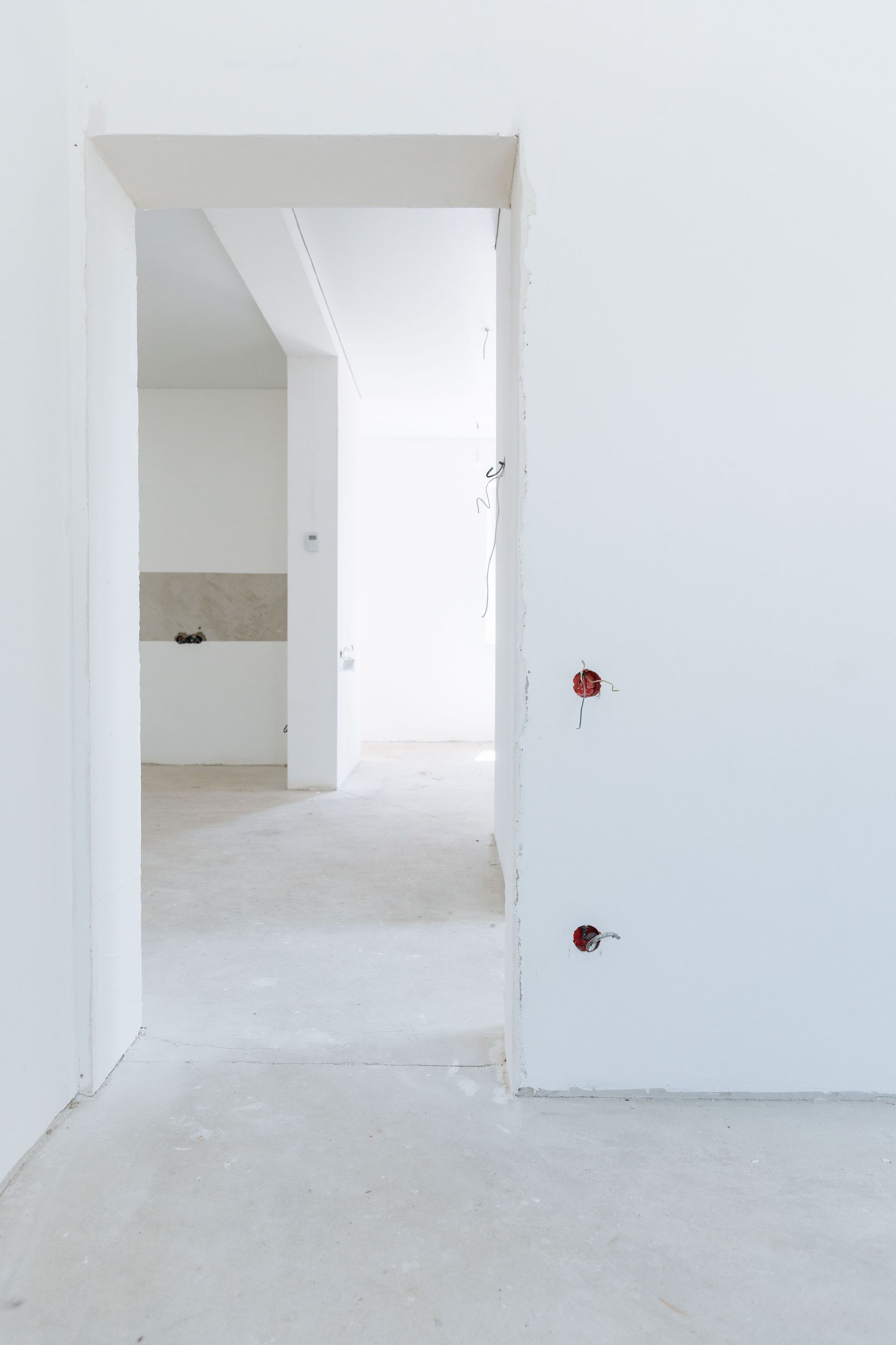 Empty white interior hallway under construction with open doorways and unfinished floors.
