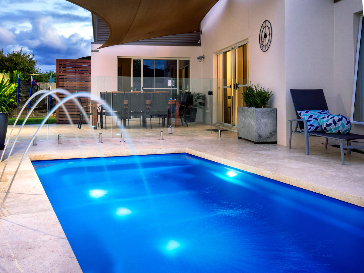 Pool with fountain jets, patio furniture, and shaded outdoor area.