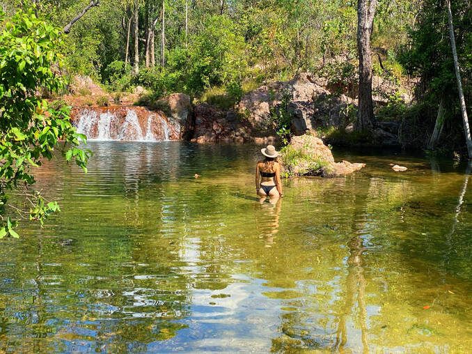 A woman is swimming in a river with a waterfall in the background.