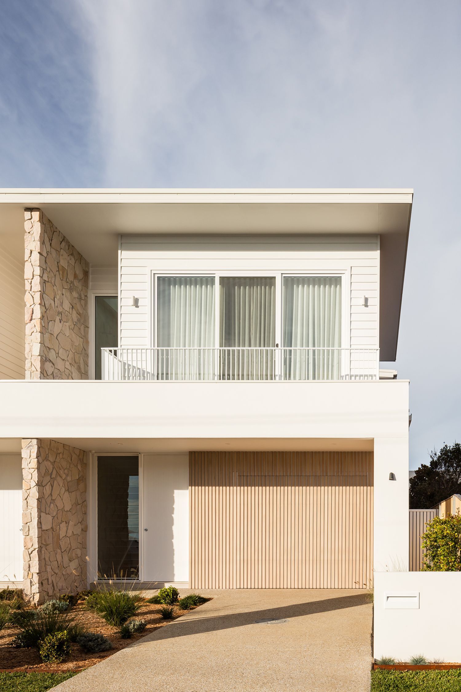A white house with a wooden garage door and a balcony.