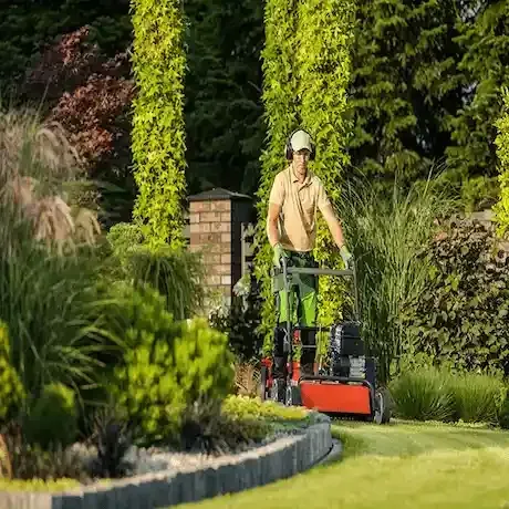 A man is mowing a lush green lawn with a lawn mower.