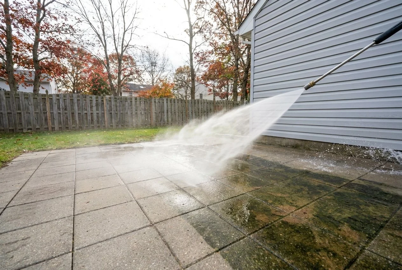 Power washing a stone patio beside a house
