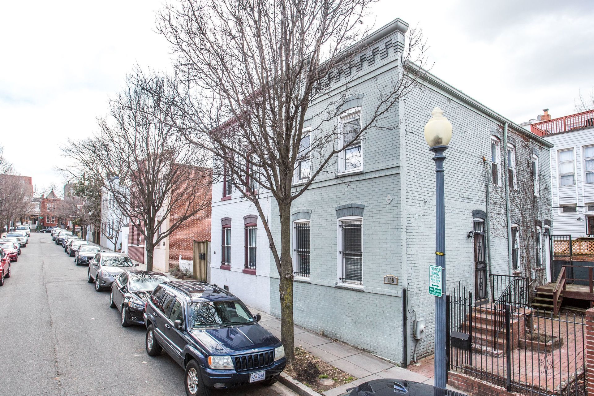 DC street a house on end is light blue row house with cars parked and trees on the street
