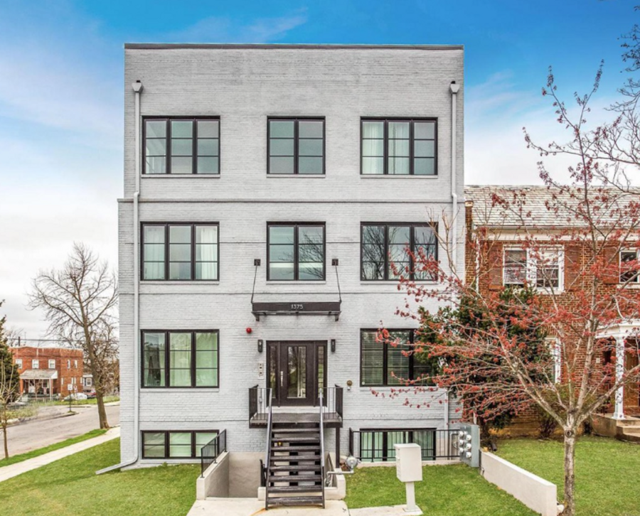 White apartment small with four floors black windows and white paint next to red house