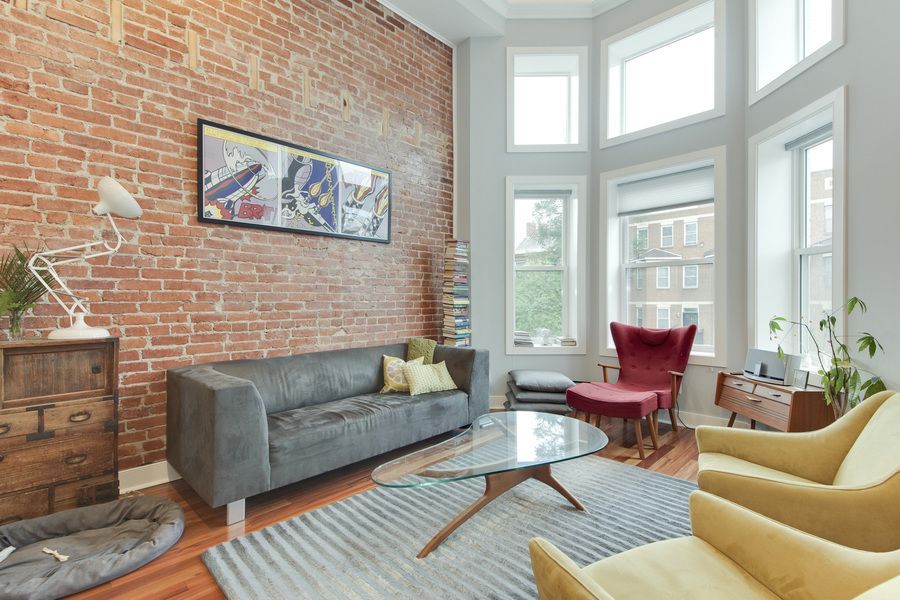 living room with high ceilings yellow arm chairs brick wall and tall bay window