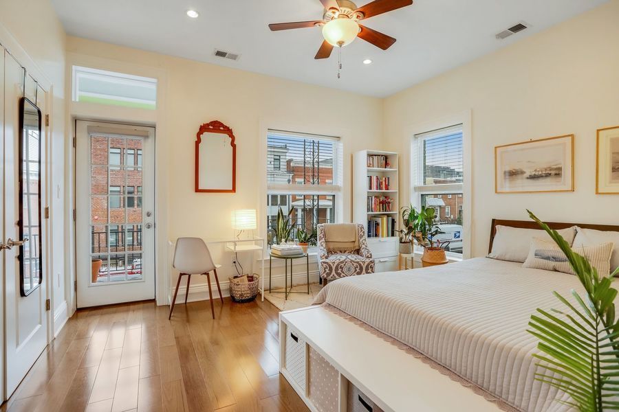 large bedroom with yellow paint wood floors two chairs built in bookcase ceiling fans and bed with table at the end