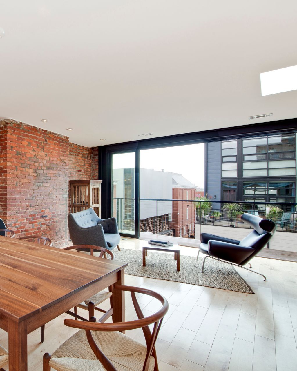 Modern interior living space with exposed brick wall, designer furniture, and large windows with balcony view.