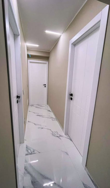 Una porta interna grigia e ruvida, incastonata in una parete bianca, con una maniglia rotonda argentata e un interruttore della luce nelle vicinanze.