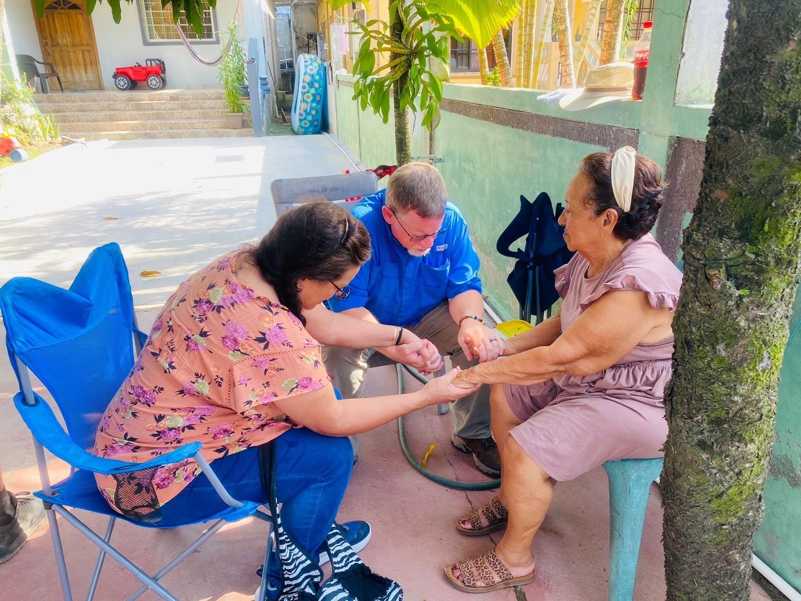 A man and two women are sitting at a table holding hands.