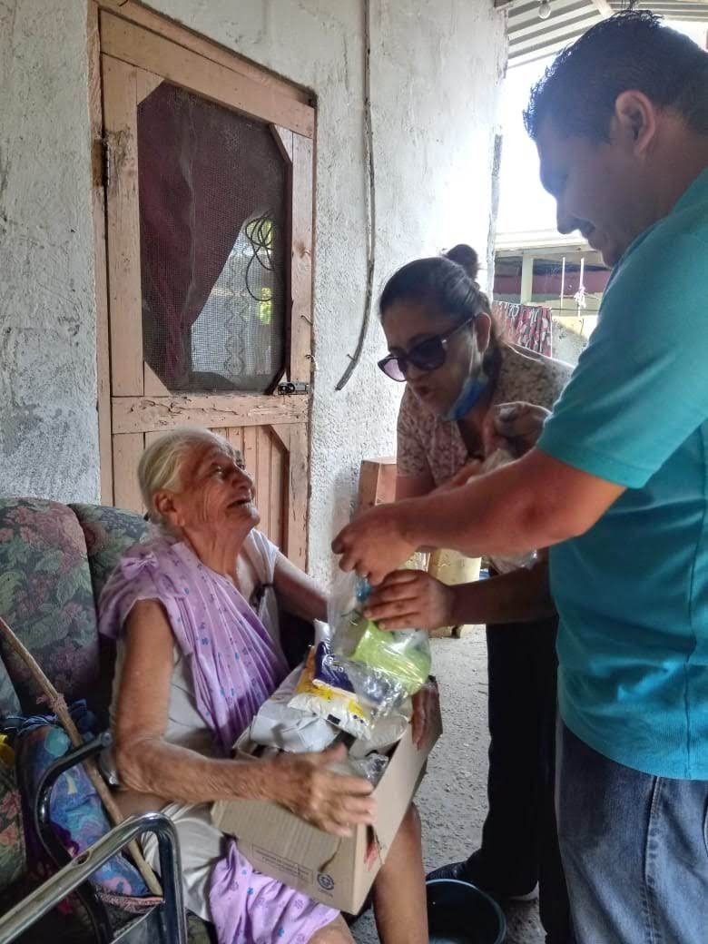 An elderly woman in a wheelchair is being helped by a man and a woman.