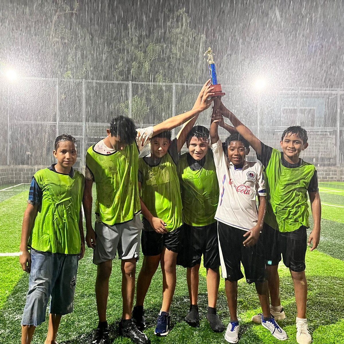 A group of young boys are holding a trophy in the rain.