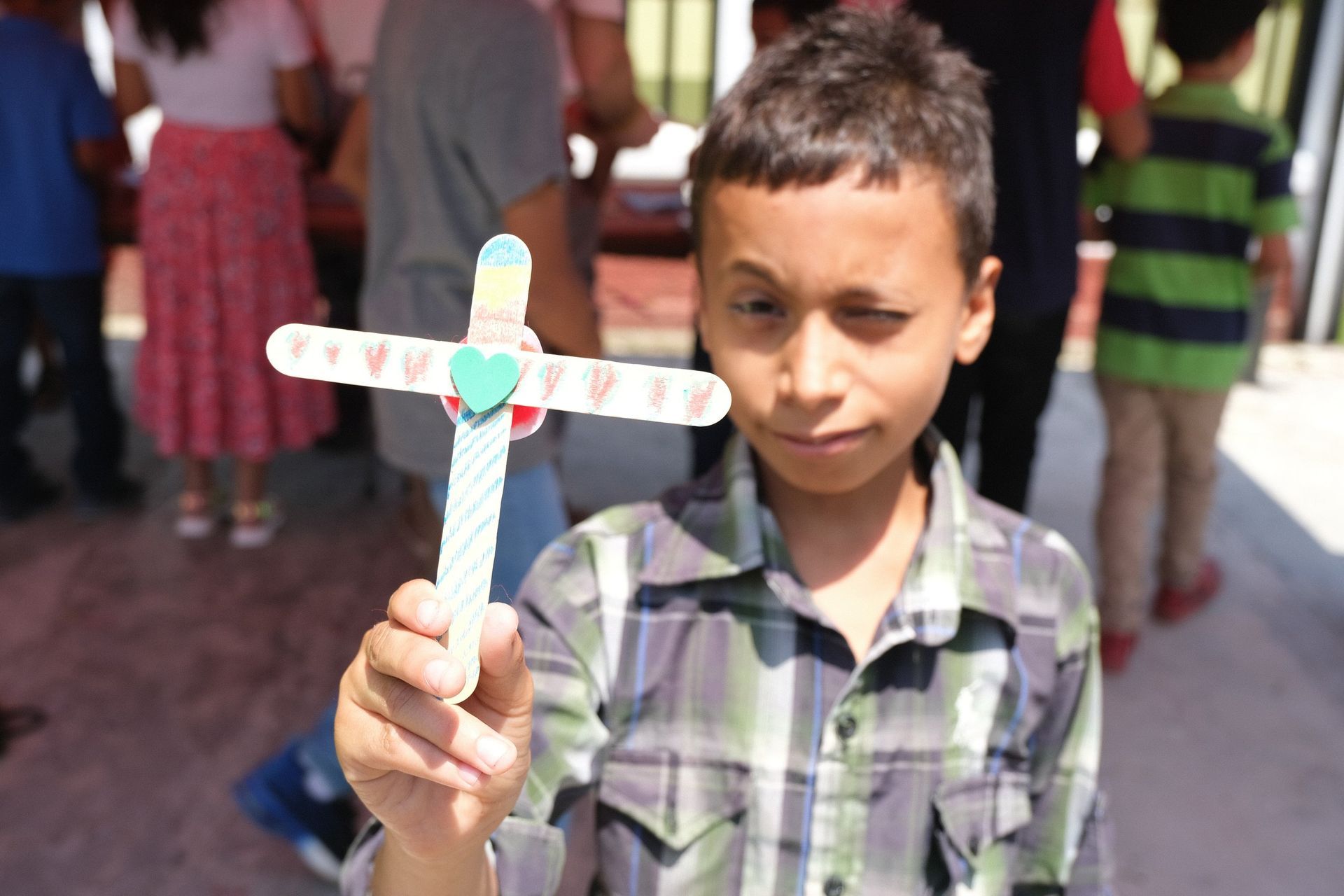 A young boy is holding a cross made out of popsicle sticks