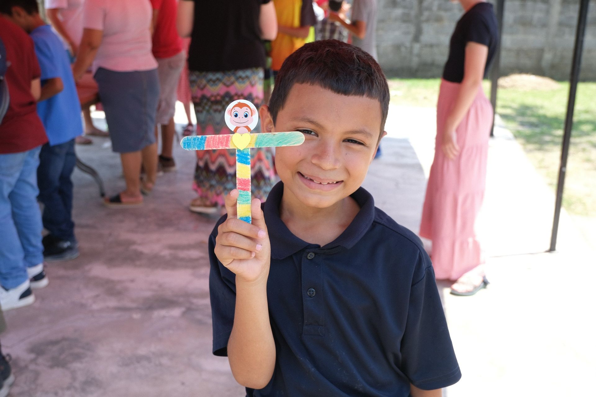 A young boy is holding a colorful cross in front of his face.