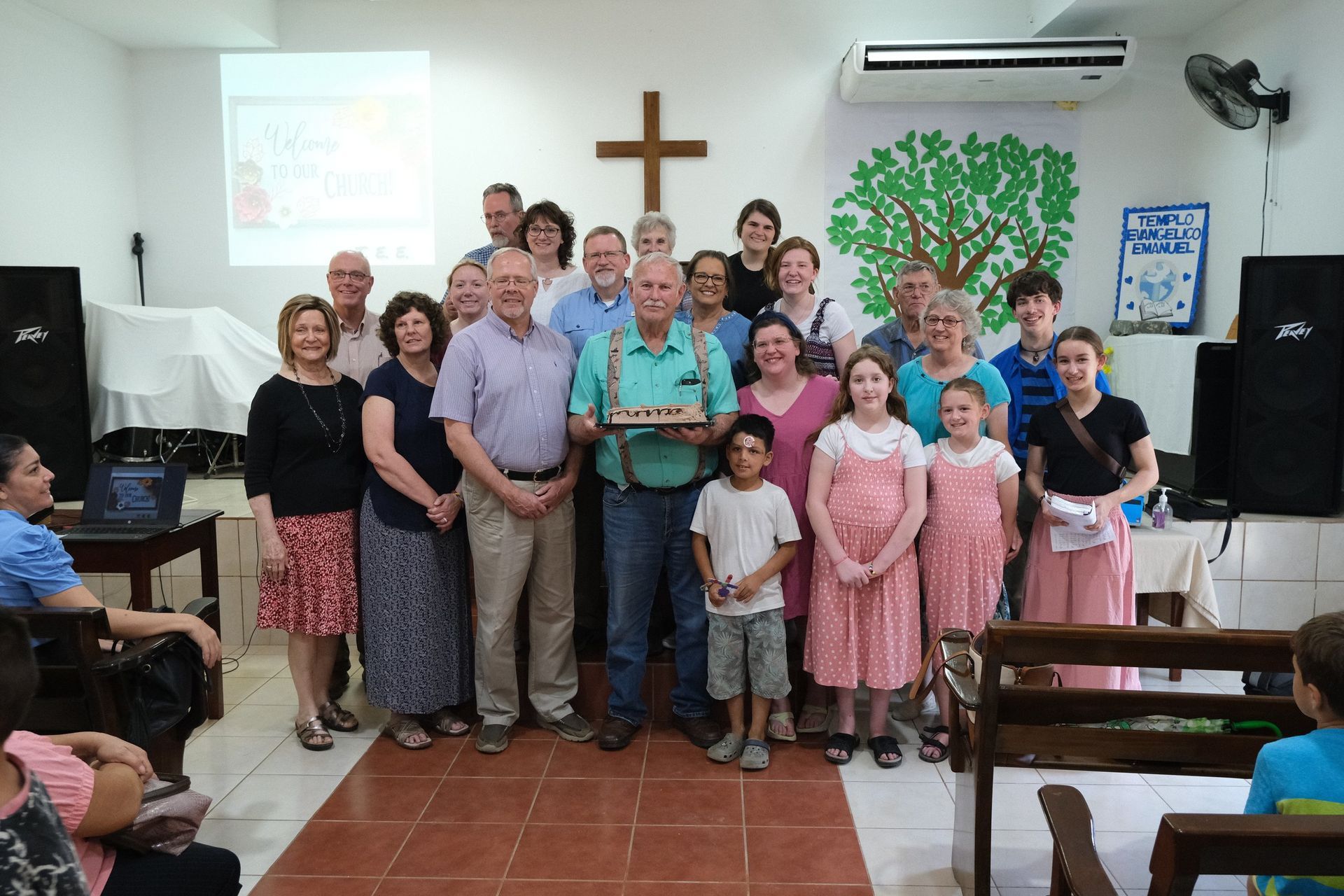 A group of people are posing for a picture in a church with a cross on the wall.