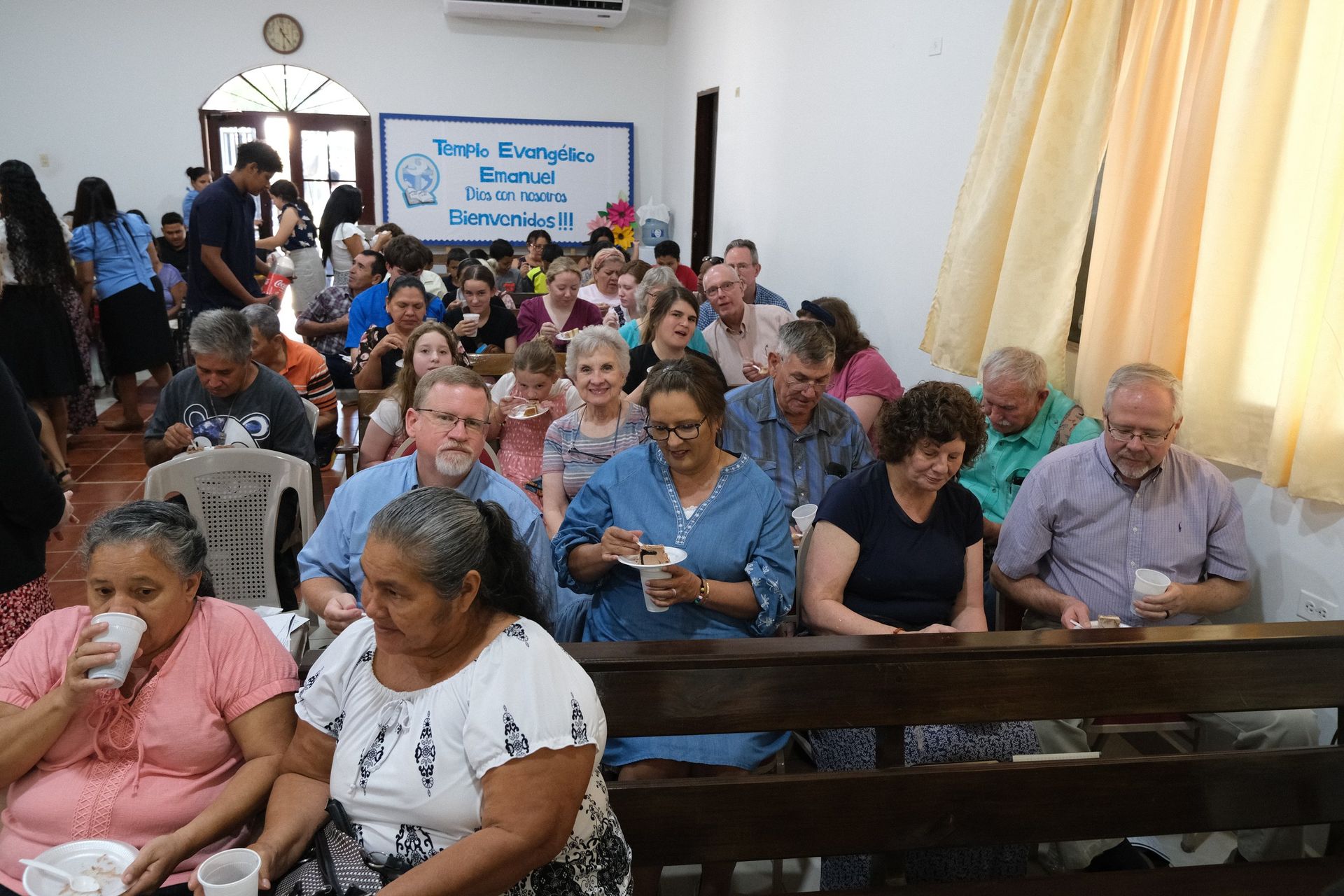 A large group of people are sitting in a church eating and drinking