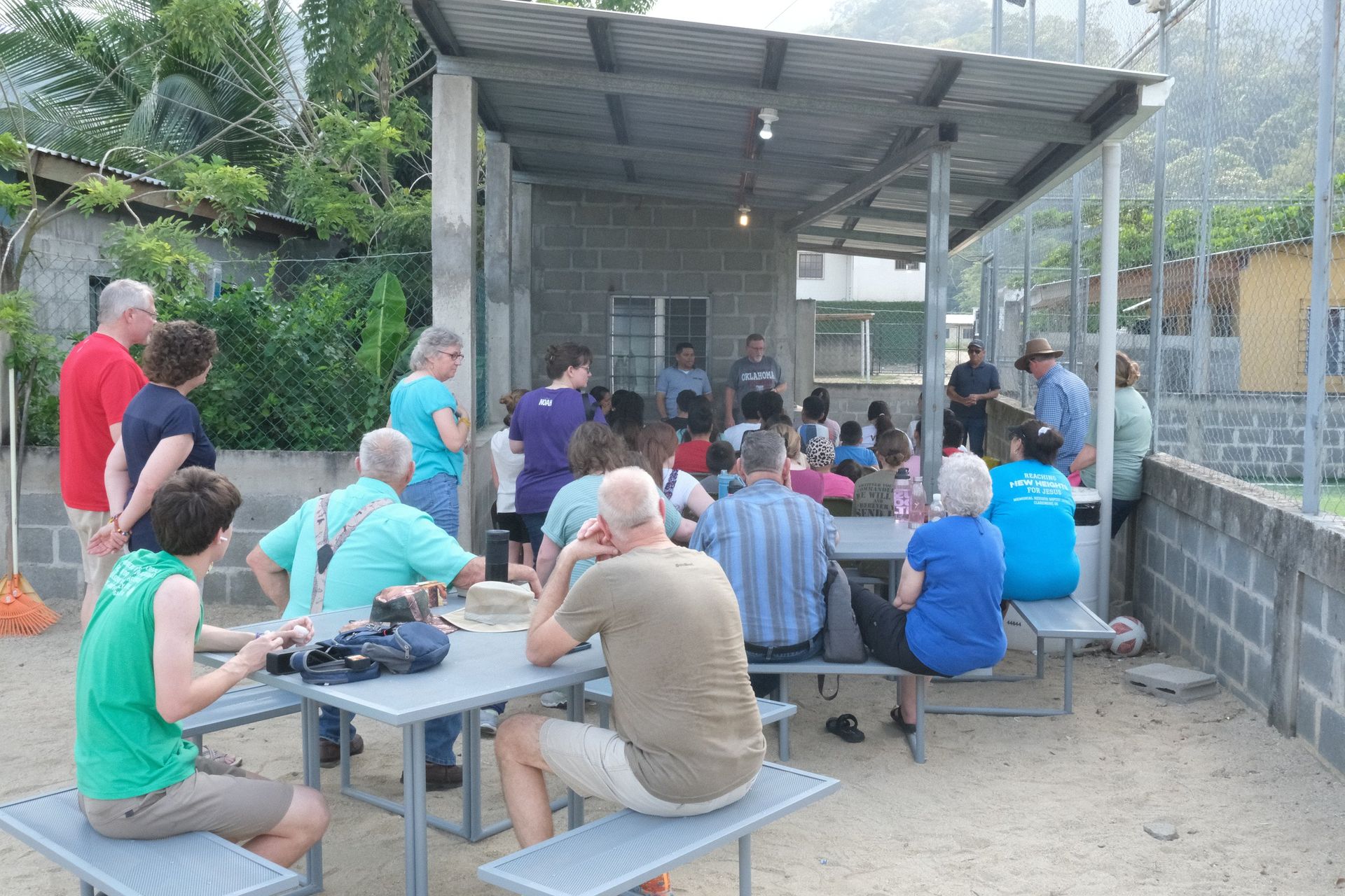 A group of people are sitting at picnic tables under a canopy