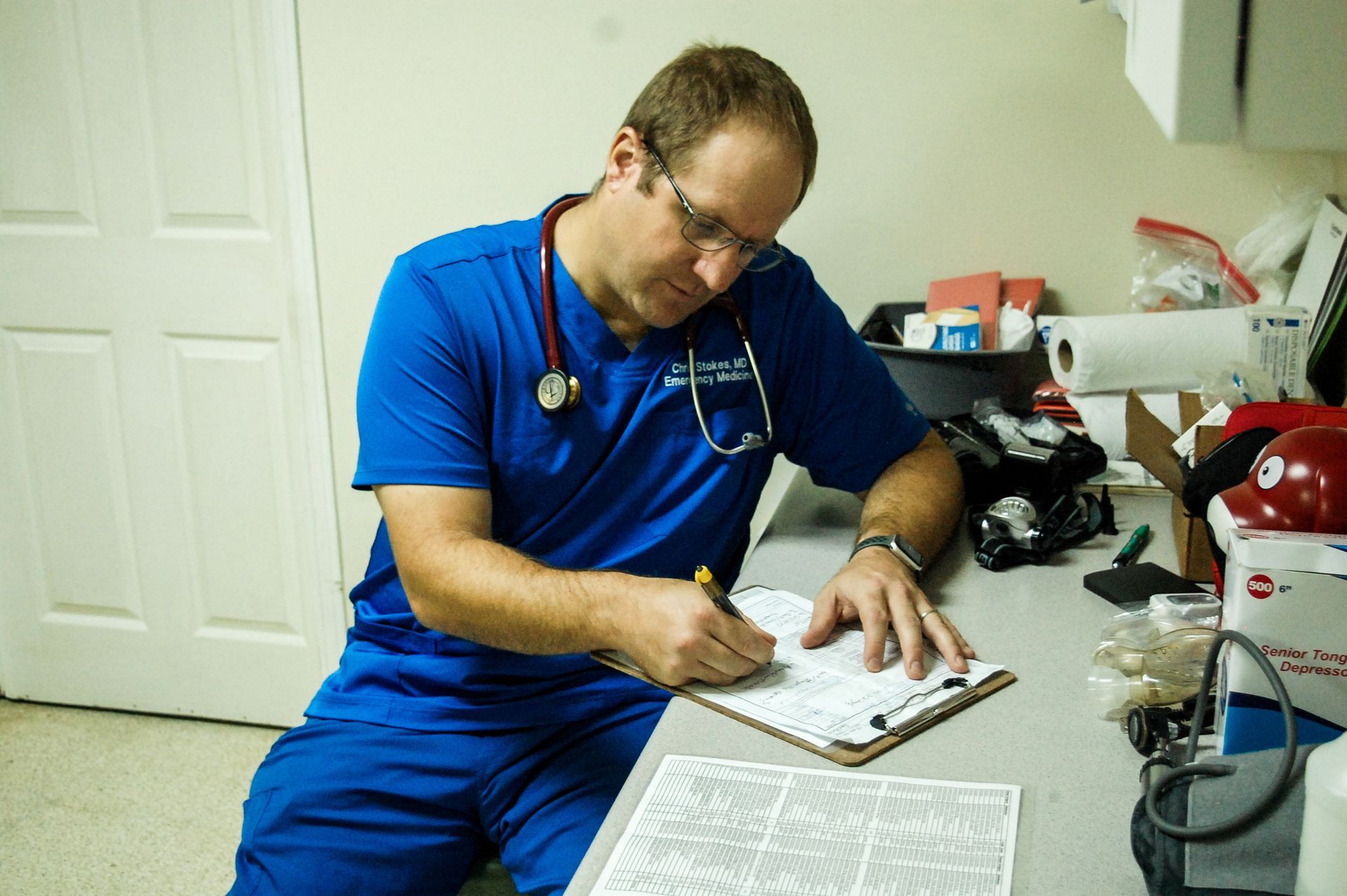 A doctor is sitting at a desk writing on a clipboard.