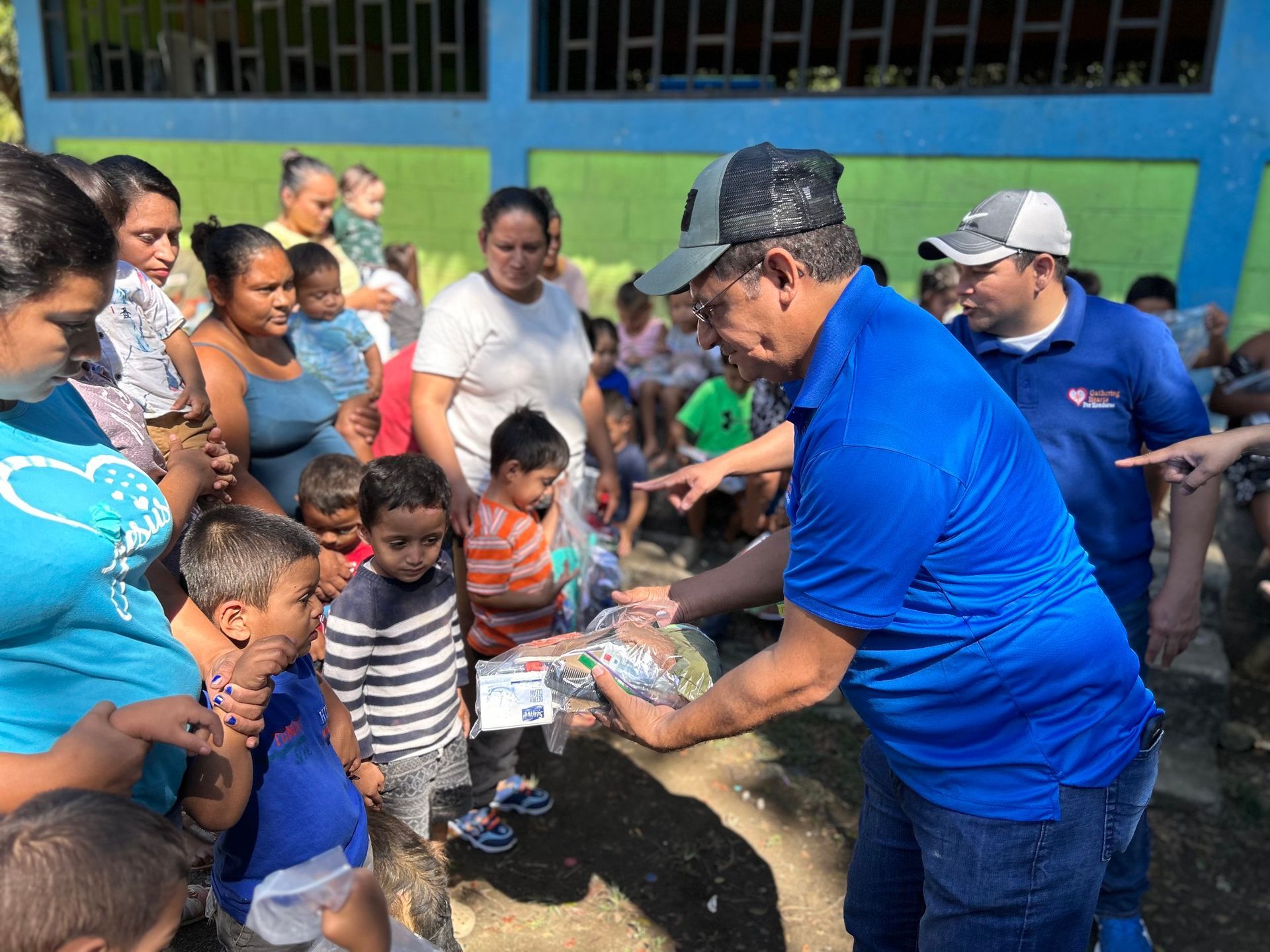 A man in a blue shirt is giving a gift to a group of children.