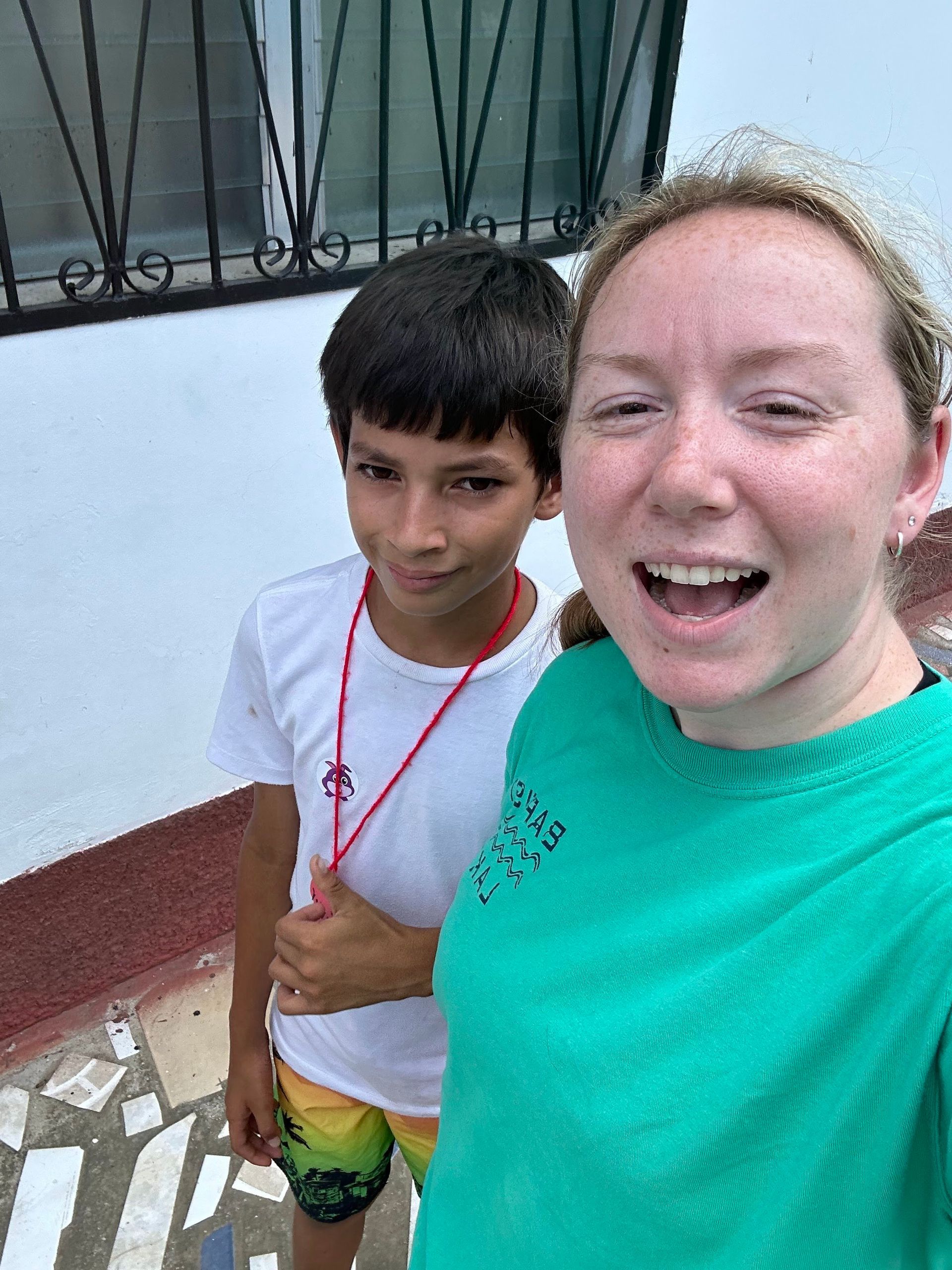 A woman in a green shirt is standing next to a boy in a white shirt.