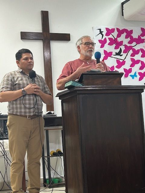 Two men standing in front of a podium with a cross in the background